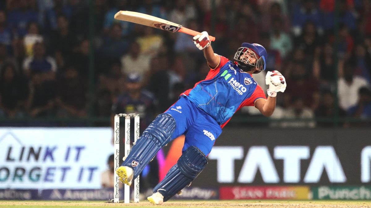 Rishabh Pant, wearing blue and red, swings the bat wildly in an IPL 2025 cricket match