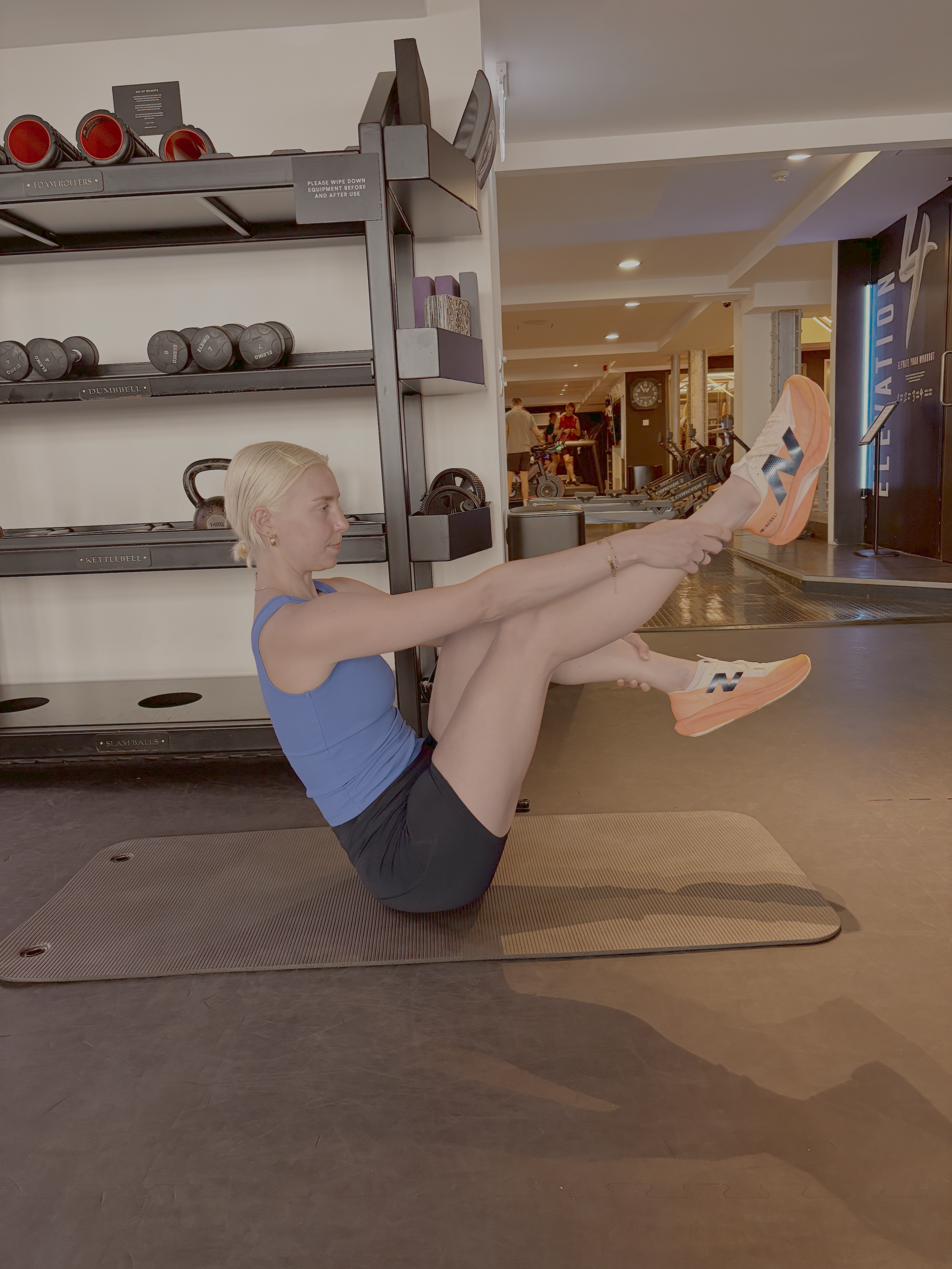 A woman practicing a seated Pilates position in a gym setting