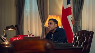 Adeel Akhtar as Prime Minister Eaves, sitting in a leather chair at a desk with a U.K. flag behind him, in 'Black Doves.'