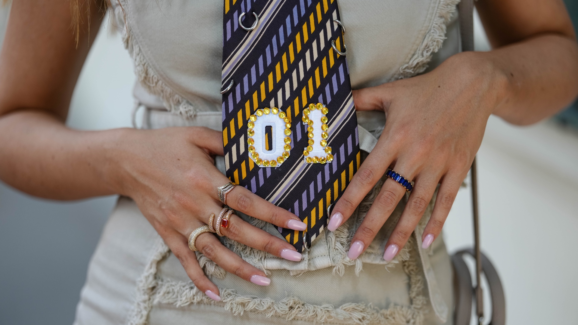 woman with neutral nails and a colorful tie and rings