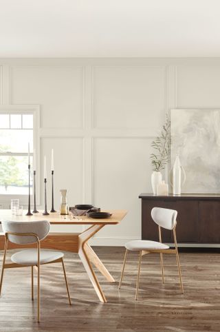 dining room with light grey panelled walls, light wood dining table and white chairs, dark wood chest of drawers