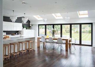 a large galley kitchen extension, with white countertops and cabinets, a large island with wooden stools, and a large wooden dining table leading out onto bifold doors