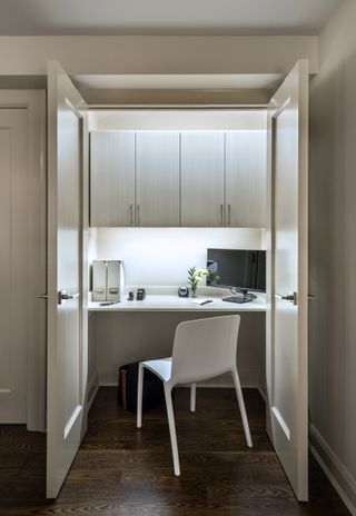 closet home office with white storage, doors, walls and chair, dark wood fiooring, lighting