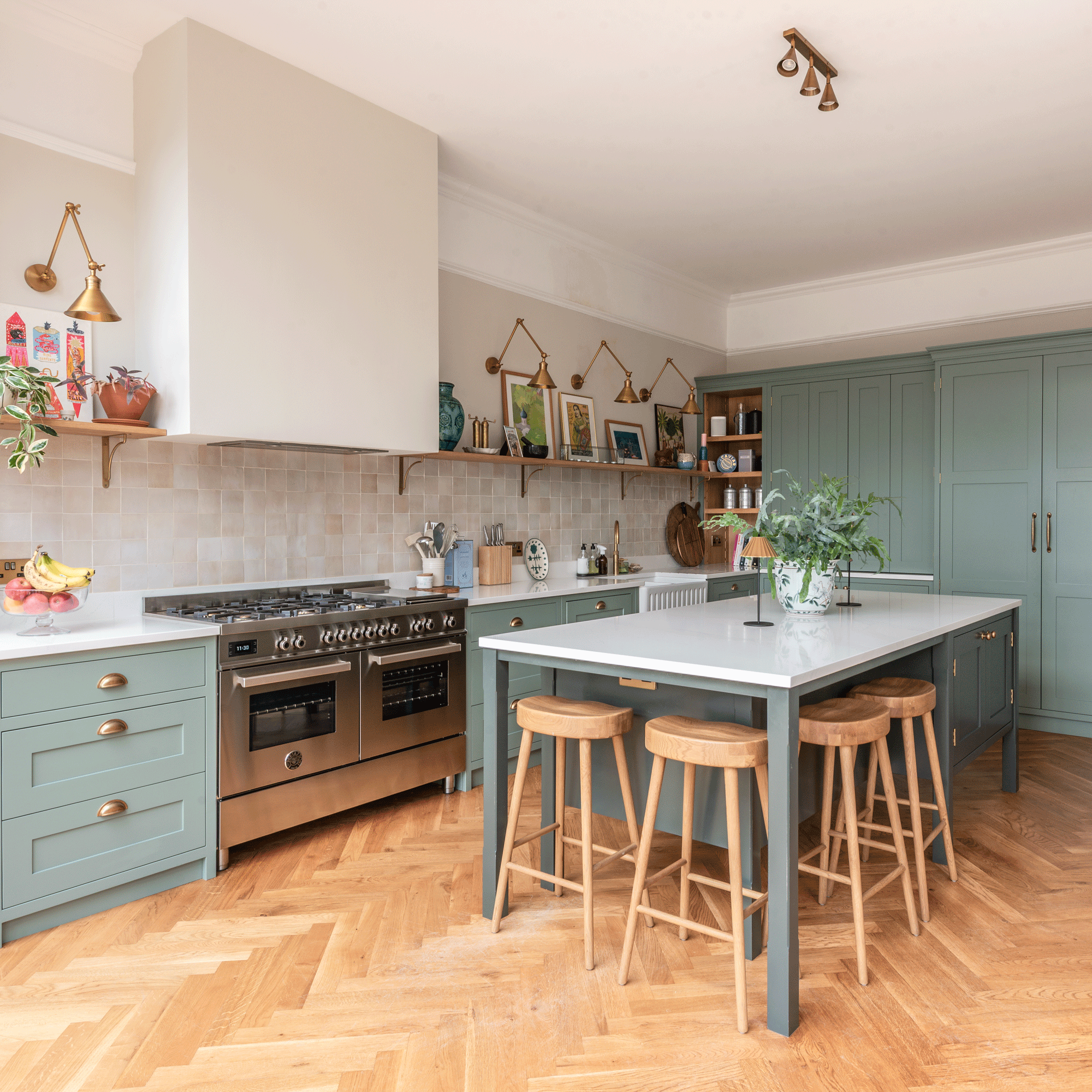 a kitchen with sage green cabinets and a fluted double Belfast sink with brass hot water tap, tiled splashback and open shelving, and a kitchen island with breakfast bar and stools