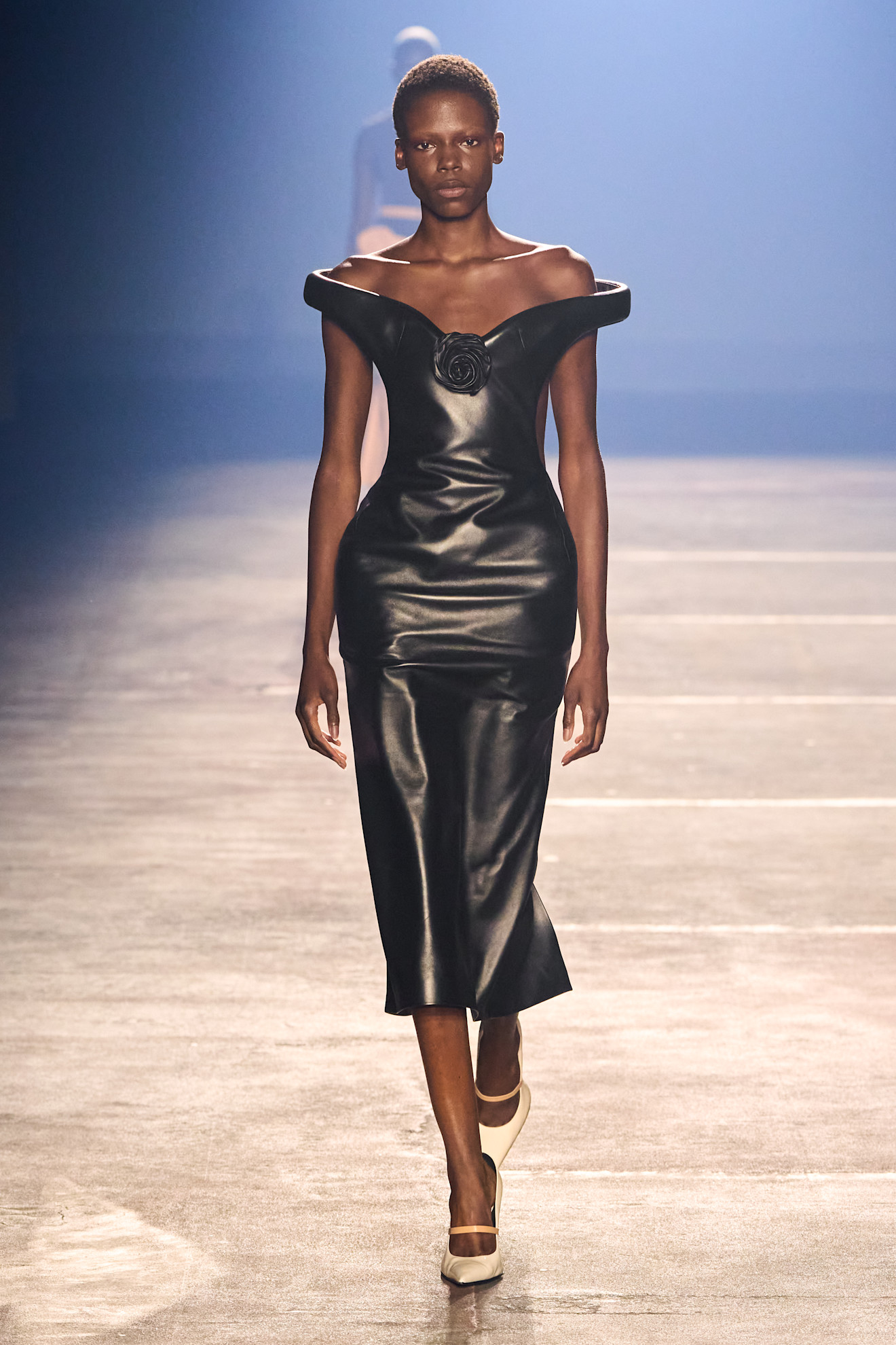 a model on the Mugler runway wearing an off the shoulder dress with a rosette