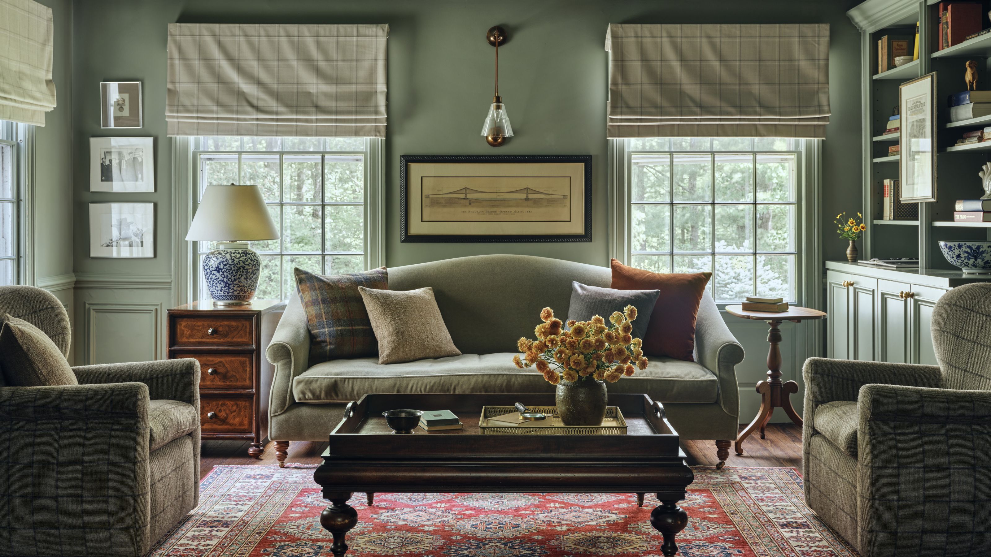 a library room color drenched in a warm green with matching sofa, bookcases, three windows and two plaid armchairs