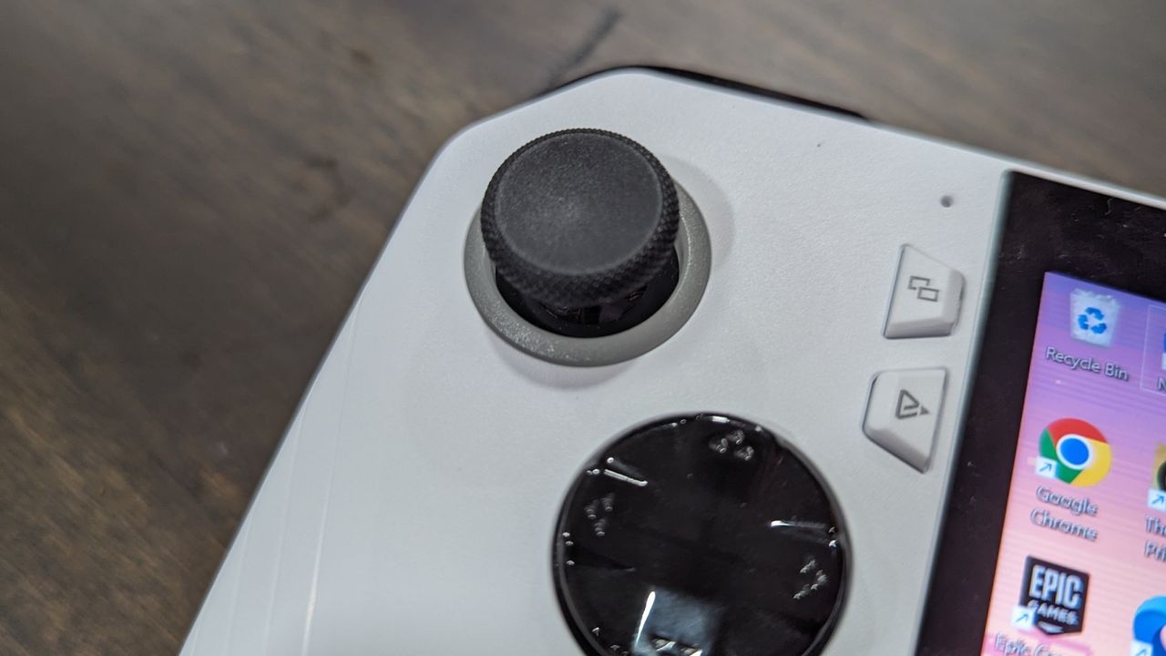 Asus ROG Ally Z1 on a brown table, highlighting the analog stick and d-pad on the left side.