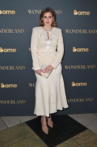 Princess Beatrice wearing an ivory dress with bows standing in front of a gray background