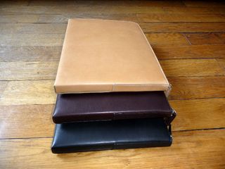 Three different coloured leather bags, stacked on a wooden floor