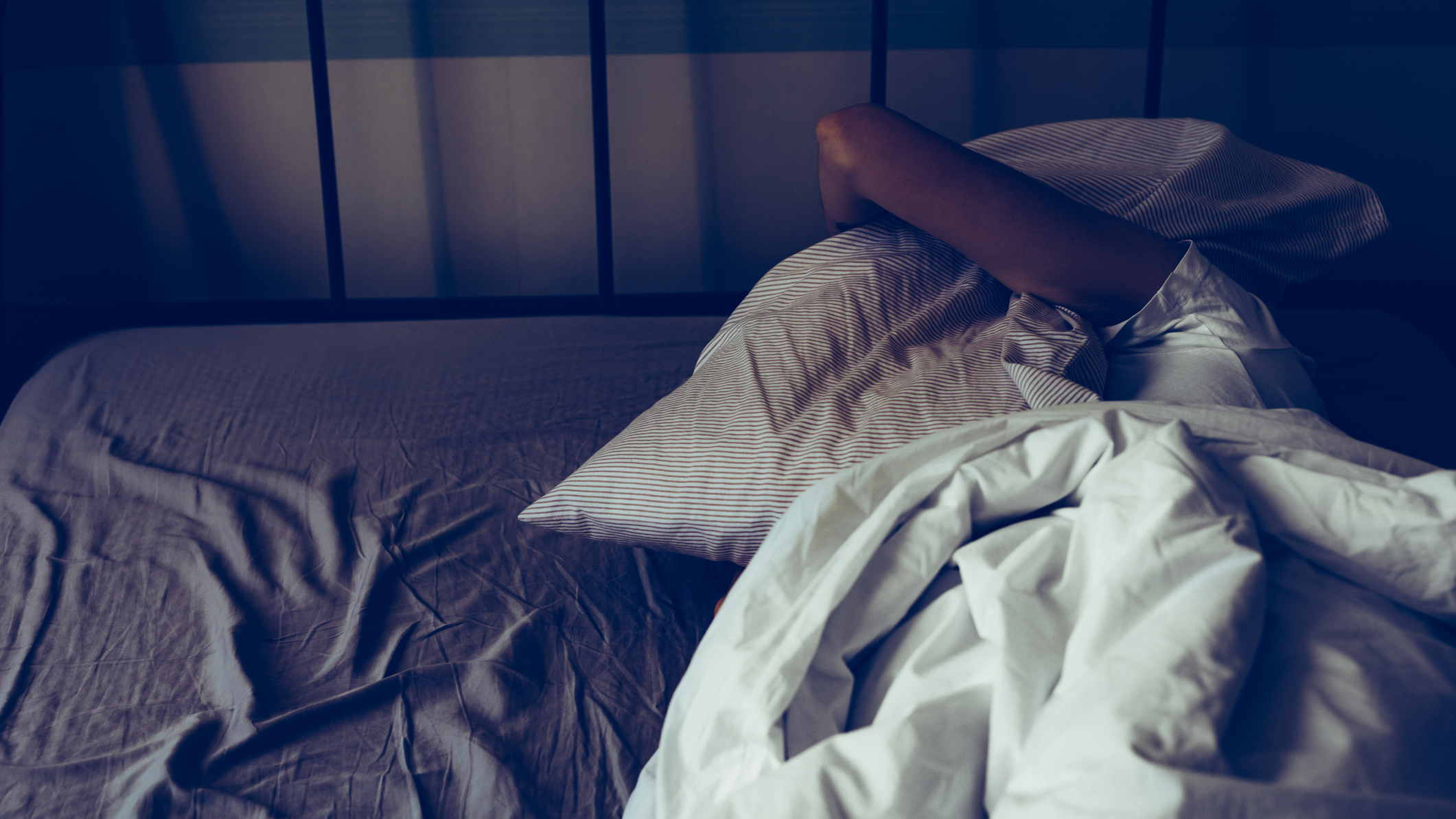 A woman wakes up at night and places a pillow over her head in frustration because she can't sleep