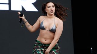 Muller in a bikini top and camouflage pants on the stage with a microphone