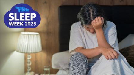 A woman is sat on the end of her bed with her head in her hands as she can't sleep because of nighttime anxiety