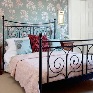 black iron bed with pink throw in front of floral wallpaper