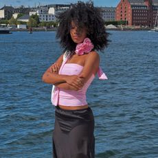 Image of a woman with a curly, long afro posing in front of a body of water.