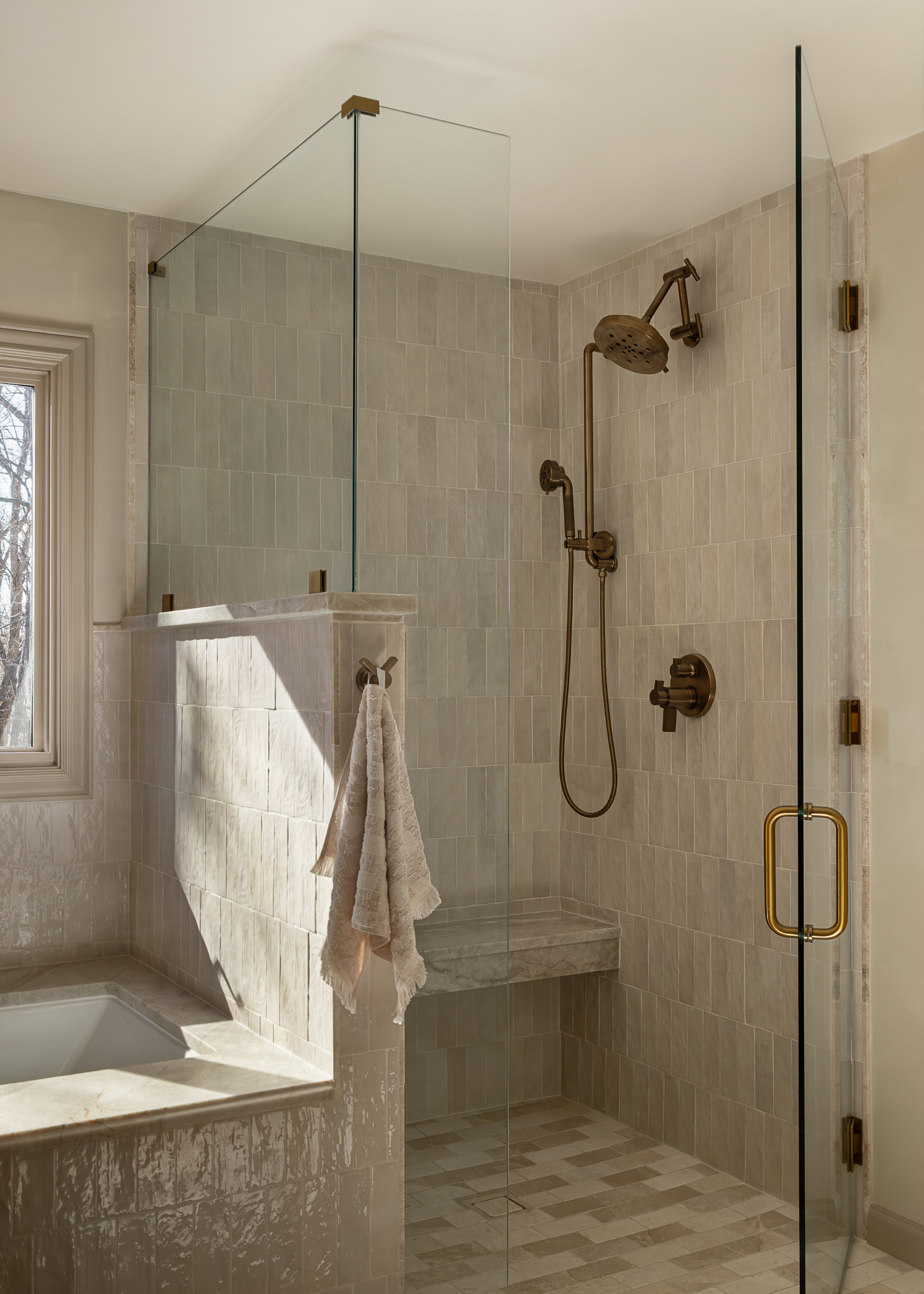 a white tiled glass enclosed shower room with a tiled shower bench and aged brassware