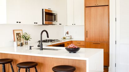 Learning how to update an outdated small kitchen is always useful. Here is a white small kitchen with light wooden cupboards, white cabinets with a silver microwave within it, a sink, and a white rectangular kitchen