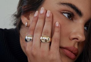 Woman wearing gold and silver rings while holding face in her hand.