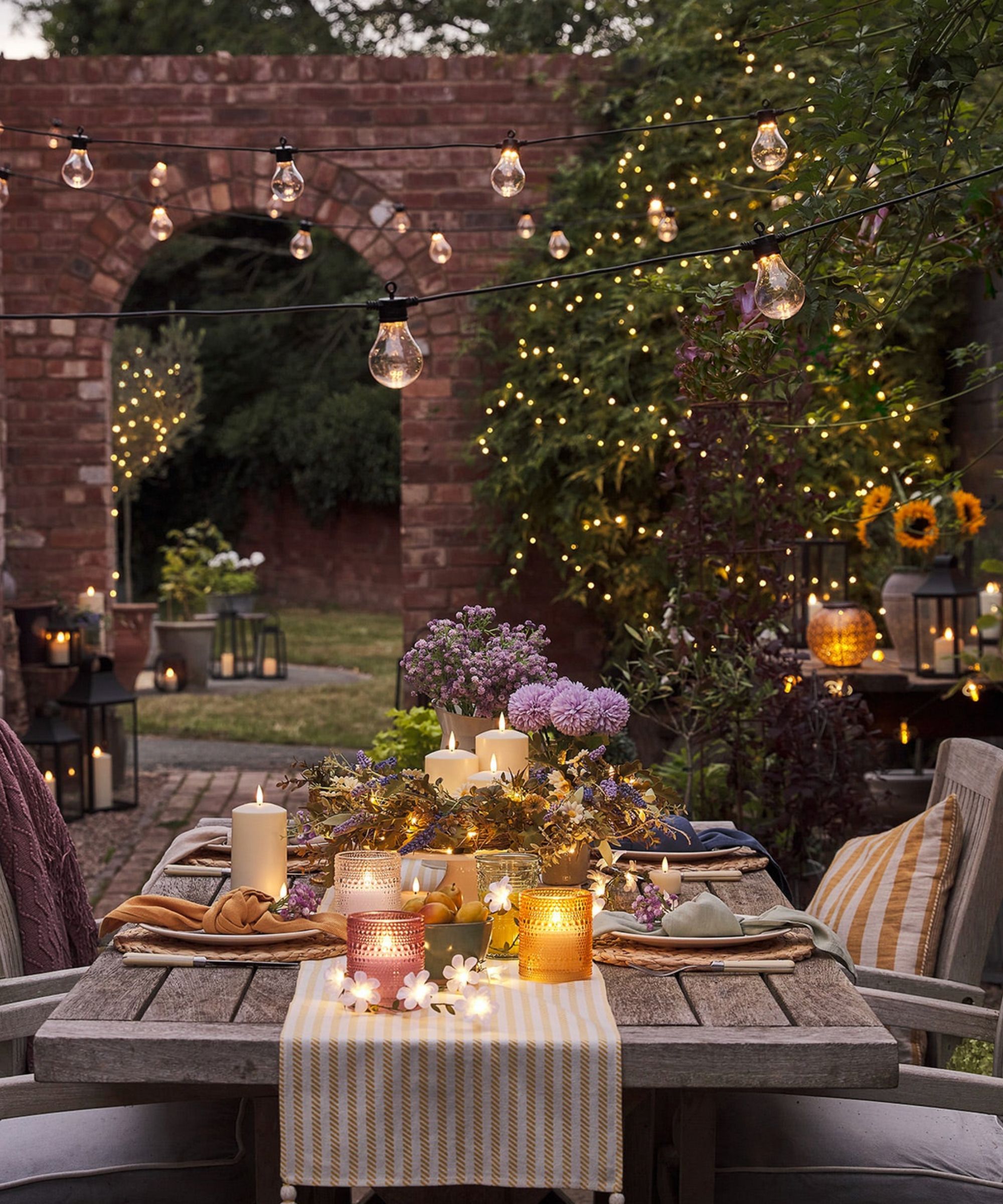 Outdoor table decorated with flowers and candles, and festoon lights overhead