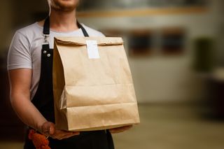Restaurant employee holding brown takeout bag