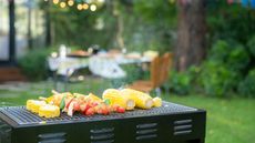 An example of where to place a grill, a charcoal grill cooking corn and kebabs away from a table