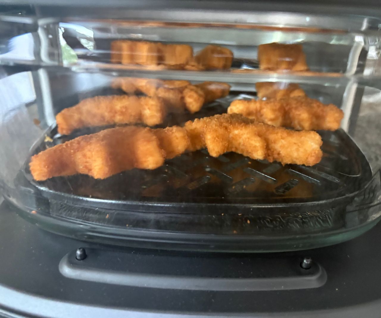 The Cuisinart glass air fryer on a granite countertop, viewed from the side with dino nuggets inside.