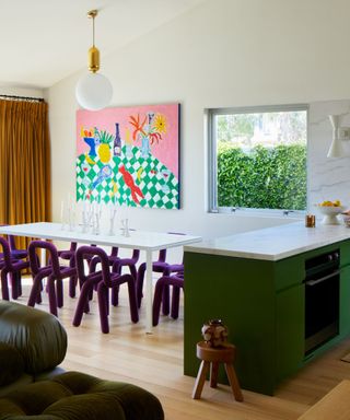 neutral kitchen diner space with green cabinets and purple dining chairs and vibrant artwork