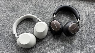 Bowers & Wilkins Px8 S2 and Sony WH-1000XM6 headphones next to each other on a grey carpet.