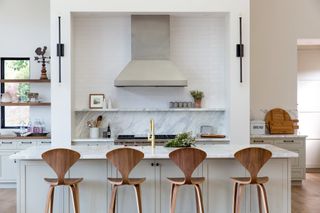 kitchen with marble splashback and white island with wooden bar chairs