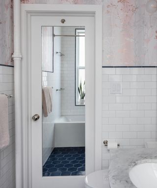 Bathroom with white walls, pale pink wallpaper, large mirror on door