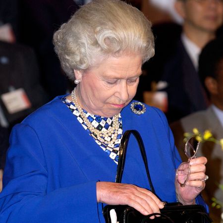 Queen Elizabeth wearing a blue coat looking down into her black handbag