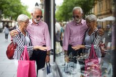 An attractive older couple pauses by a display window while shopping on the street.