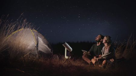 A couple use the Vaonis Stellina smart telescope to view the night sky via an iPad tablet whilst camping outdoors
