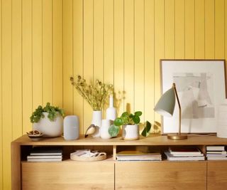 Google Nest Audio on a sideboard with vases and a yellow wall behind