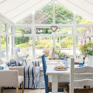 Conservatory used as a living dining space, with views of a lush garden. Roof blinds on the ceiling provide shade