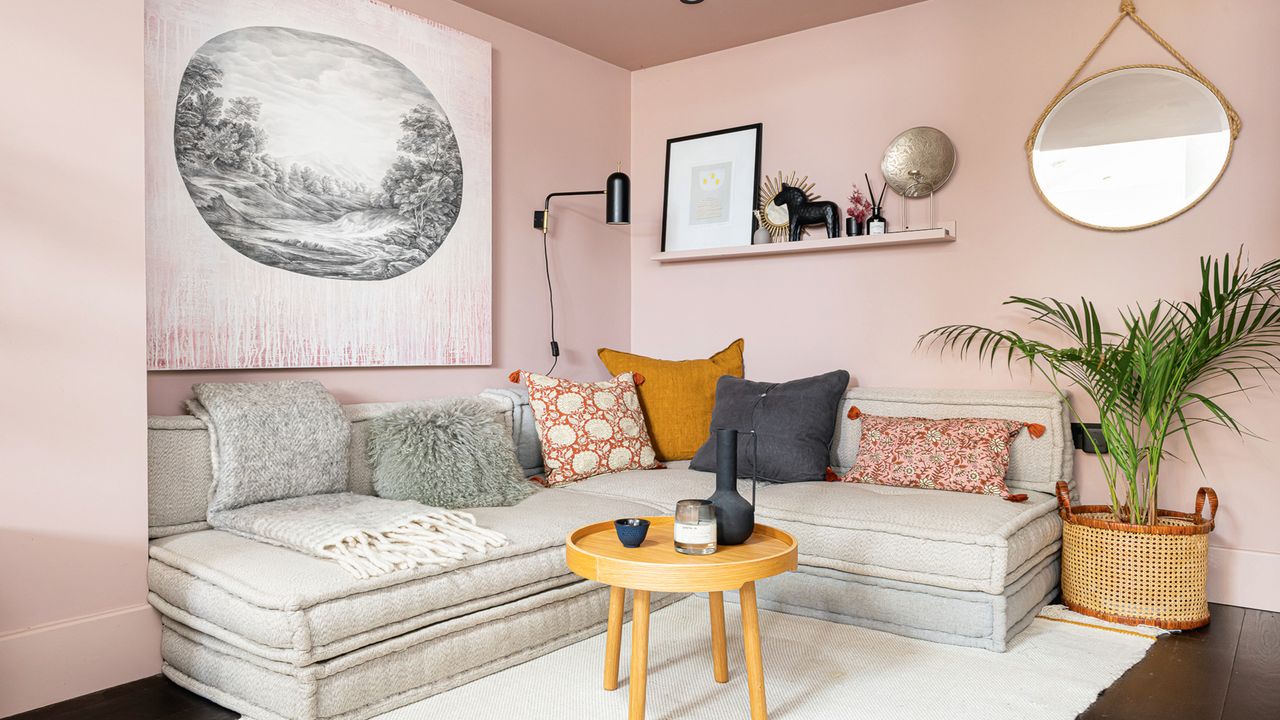 cream sofa with pillows against a pink wall with a white rug and wooden round side table