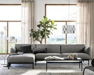 A grey 4-seater sofa with chaise longue feature by IKEA in living room with beige curtains and houseplant