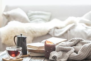 A sofa with a fluffy blanket on and a coffee table with knitted fabric, a mug of tea and a candle.