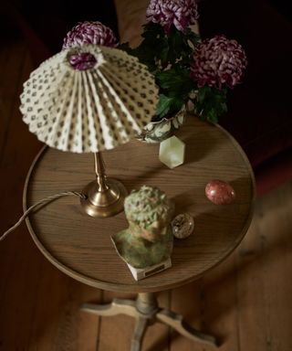 small wooden side table with a brass lamp and a patterned pleated shade sat on top with flowers and trinkets