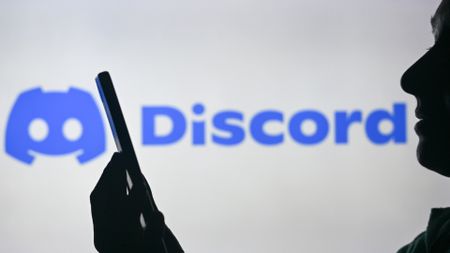 EDMONTON, CANADA - APRIL 28: An image of a woman holding a cell phone in front of the Discord logo displayed on a computer screen, on April 29, 2024, in Edmonton, Canada. 