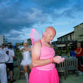 A photograph of a person in a pink fairy outfit, smoking a cigarette and looking at their phone