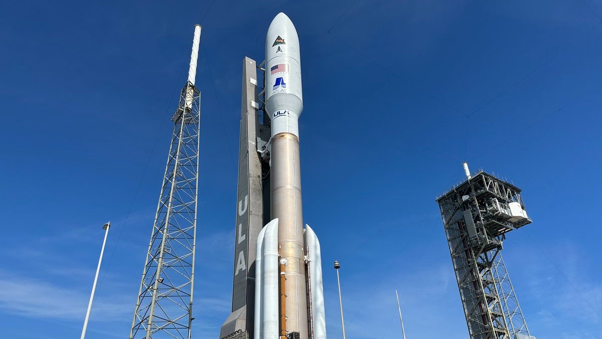 a brown and white rocket rolls toward the launch pad with blue skies in the background.