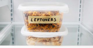 inside an open fridge showing a tuppaware box of leftover foods