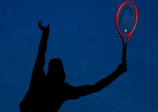 Shadow of a tennis player on the court holding a red raquet