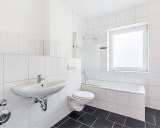 Photo of clean white bathroom with sink, bath, tiled shower, bright window and black floor tiles
