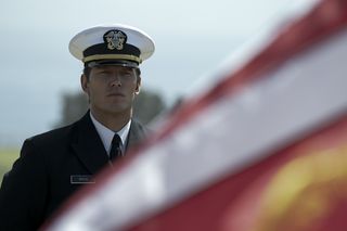 a medium shot of actor Chris Pratt in Navy uniform next to an American flag
