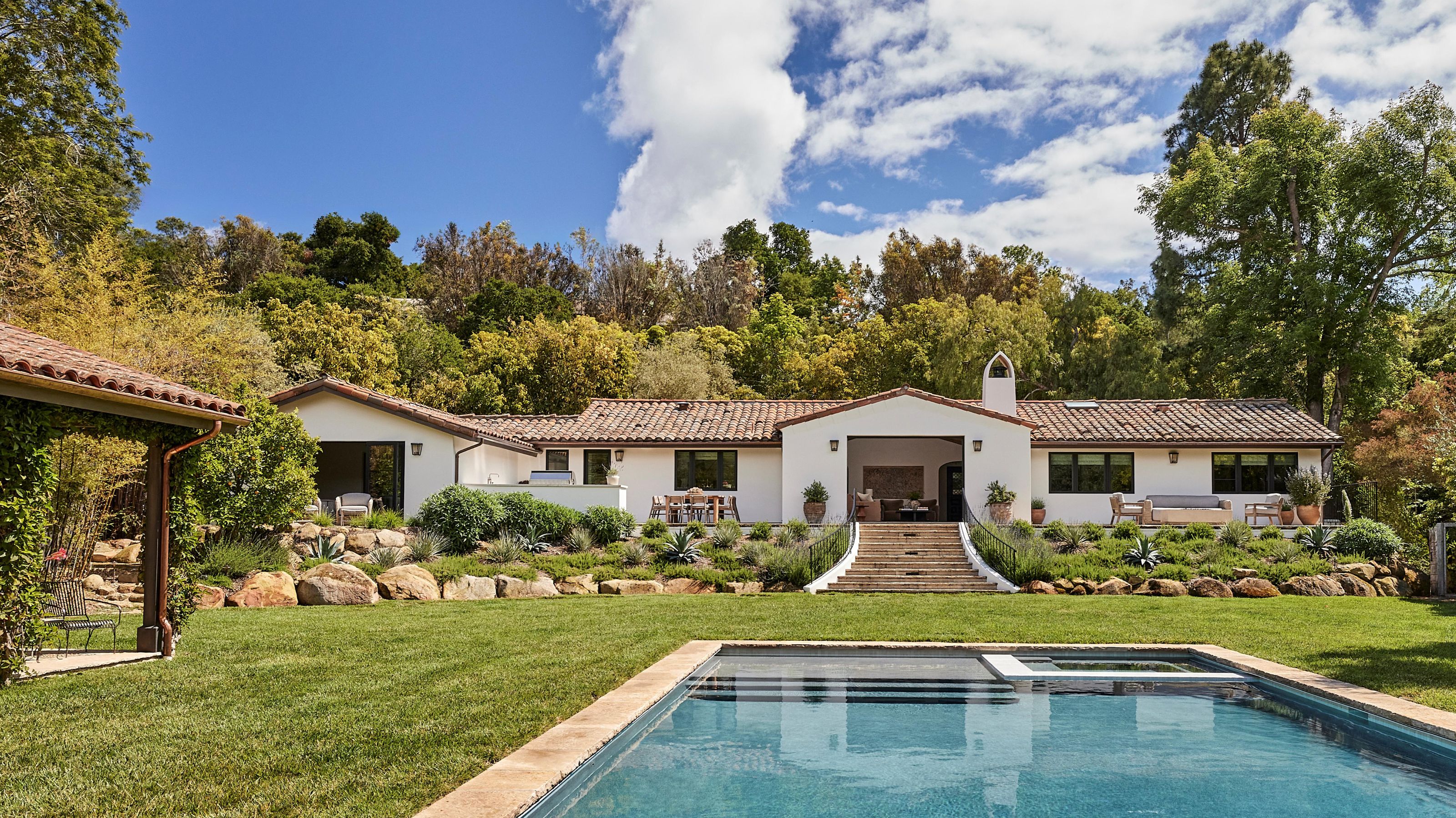 a large spanish revival white home with a separate casita, pool, and green gardens