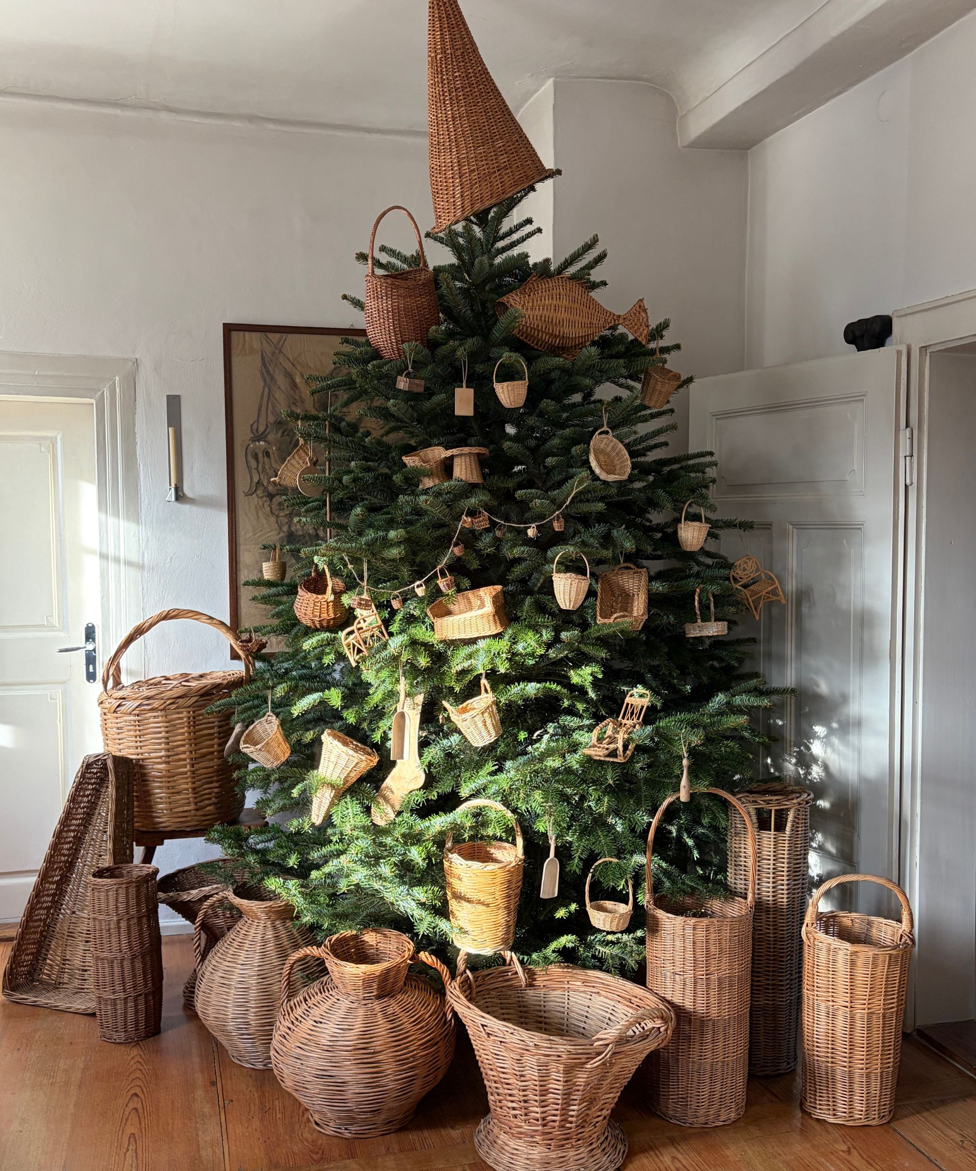 Christmas tree decorated with wicker baskets and ornaments in a white rooms with high ceilings.