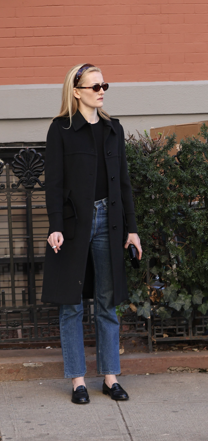 sarah pidgeon as carolyn bessette kennedy in love story wearing straight leg blue jeans and a black coat
