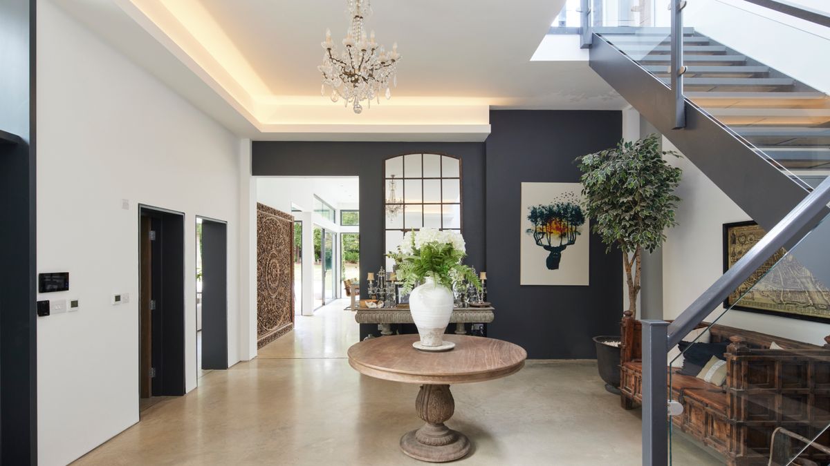 large hallway with grey and glass staircase, large stone floor tiles, LED lighting recessed in coving and glass chandelier above round wooden table