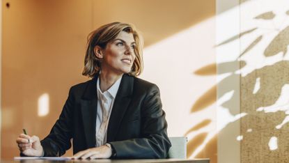 A woman looks toward the window while at her desk at work.